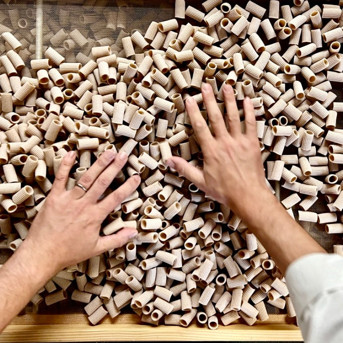 Hands interacting with a large pile of wholegrain pasta on a wooden tray from carleschi